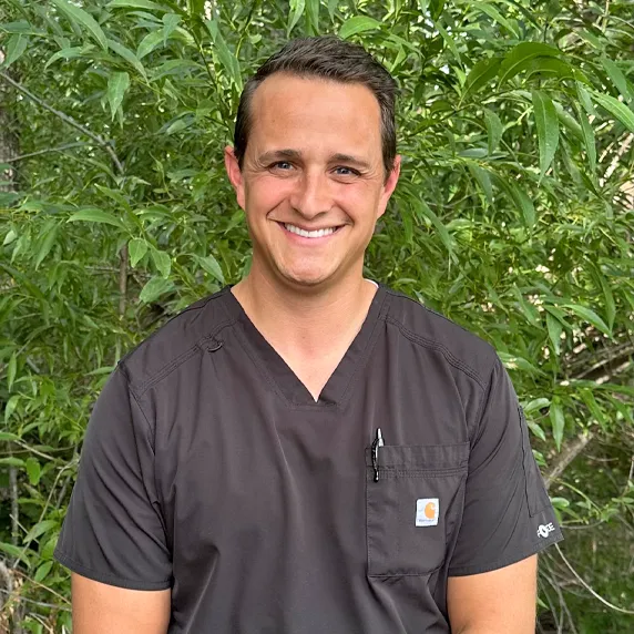 Cache Valley Dentis, Dr Burns standing in front of greenery outside in his scrubs